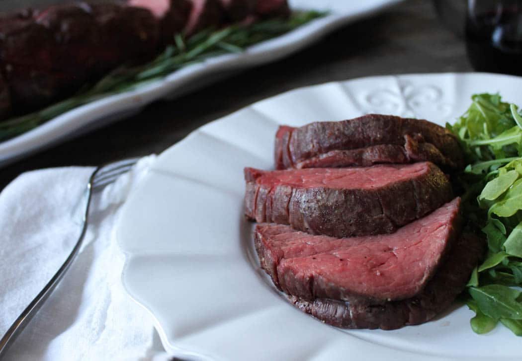 Plated beef tenderloin slices with arugula salad.