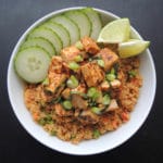 Bowl with basil tofu on a bed of stir fried quinoa garnished with sliced cucumber and lime wedges.